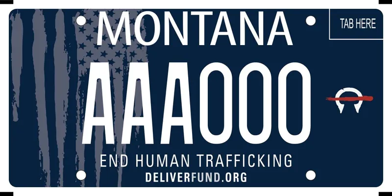 A navy blue license plate with white text. A distressed American flag in grayscale on left side of the plate. Bottom says End Human Trafficking; Deliver fund dot org.