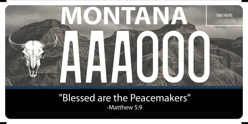 A black and grayscale license plate with white text. Backgound are rugged, rocky mountains. A buffalo skull is on left side. A solid blue line run across plate below plate numbers. Bottom text says blessed are the peacemakers. Matthew 5 9.