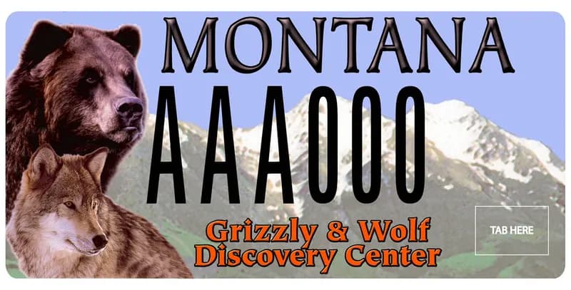 A license plate with black and orange text. Mountains in background. Grizzly bear and wolf on left side. Bottom says Grizzly & Wolf Discovery Center.