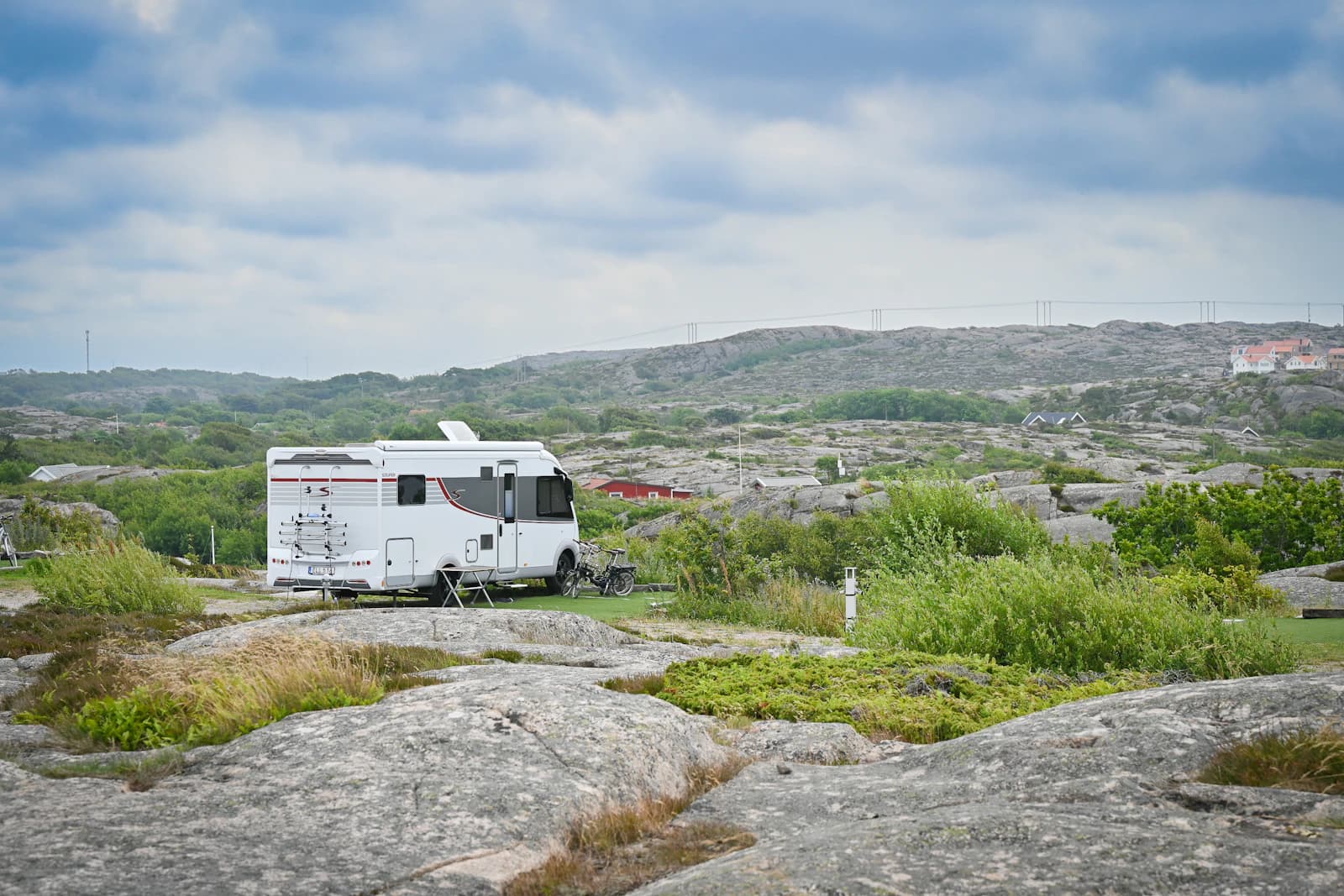 White motorhome parked on rocky terrain with hills in the distance